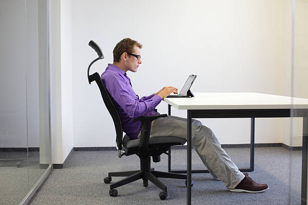 Man working on a tablet at a white desk, sitting upright in an office chair
