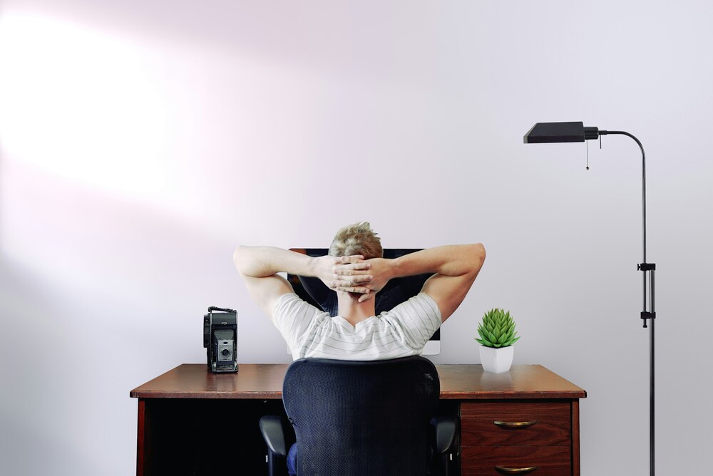 Man at a wooden desk leaning back with both hands behind his head